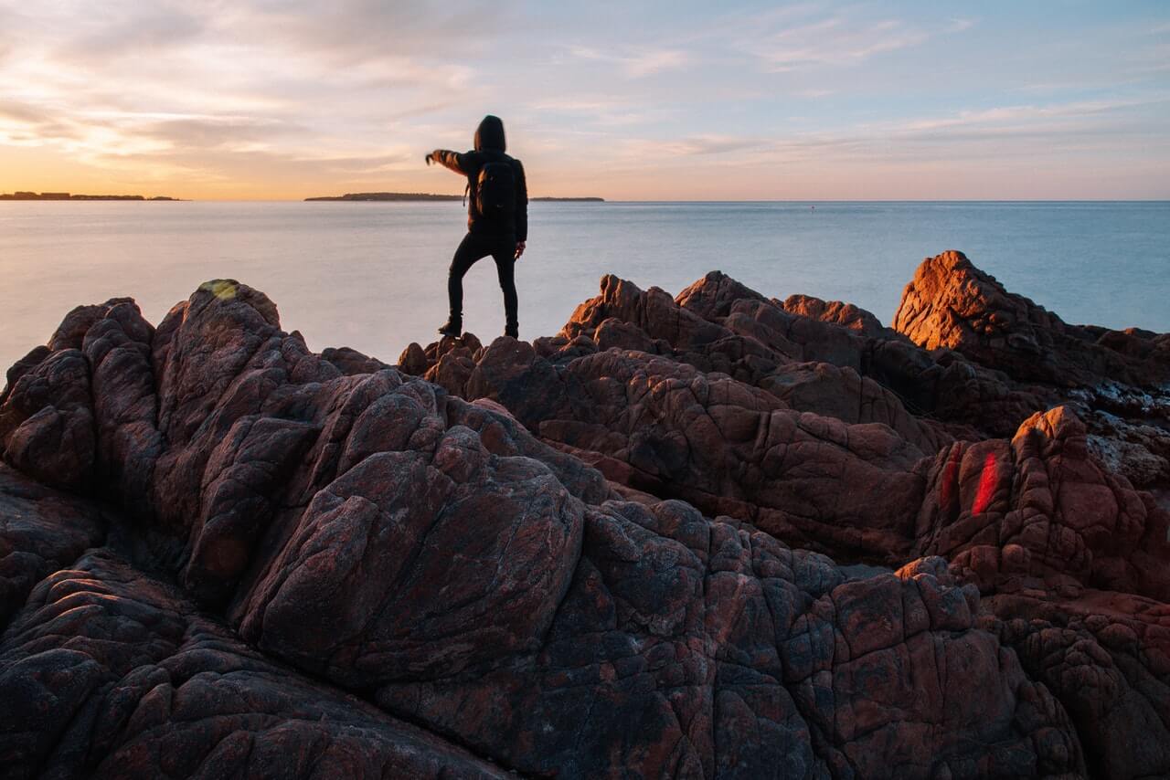 Person stands on rocks looking out to sea
